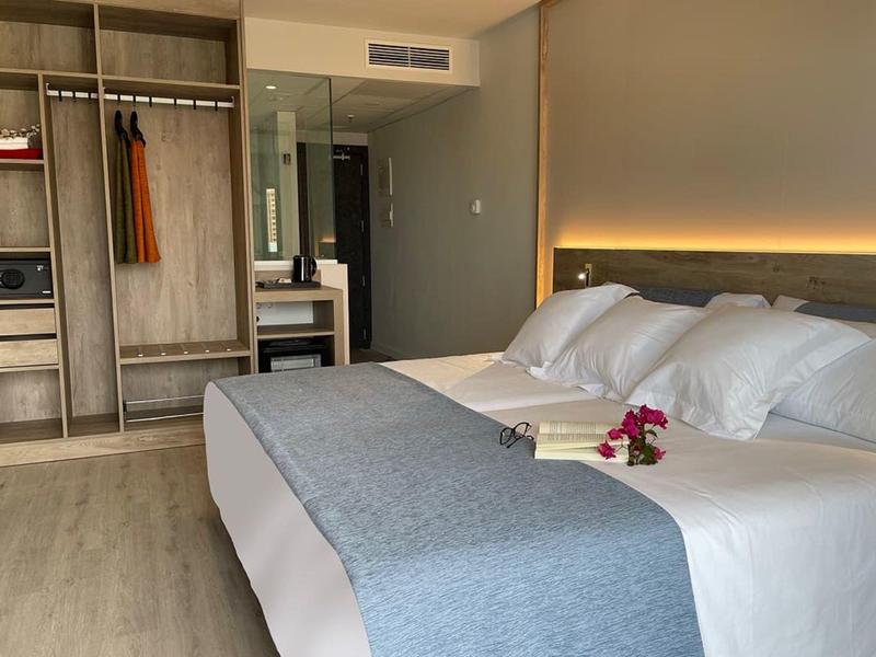 Moderne hotelkamer met groot bed, open kledingkast en bureau in warme tinten.