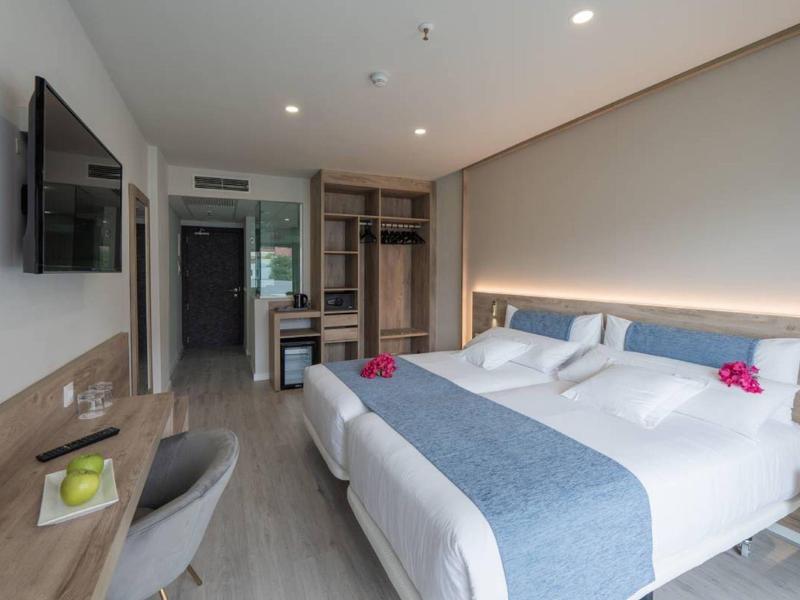 Moderne hotelkamer met tweepersoonsbed, bureau, tv en open kledingkast.