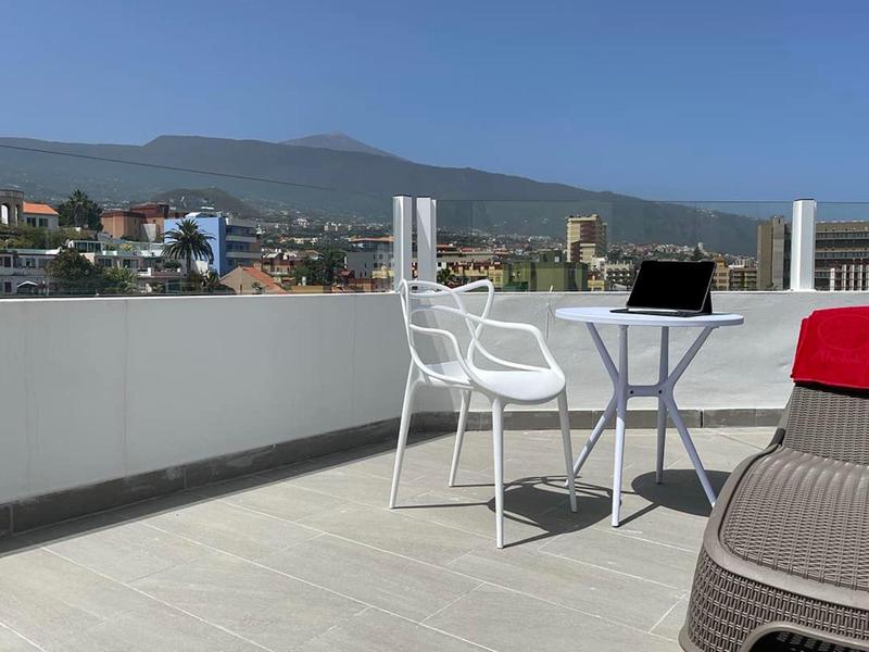 Terras met stoel, tafel en laptop, bergen op de achtergrond onder een heldere lucht.