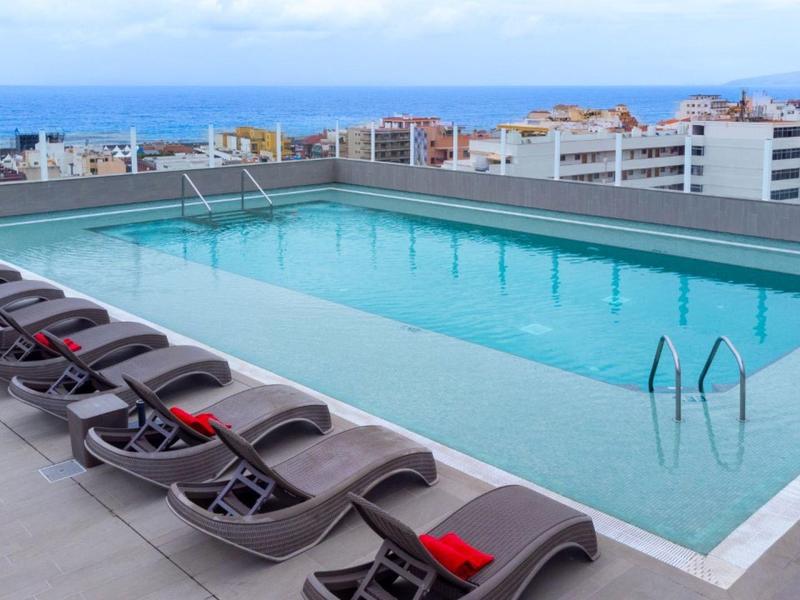 Modern zwembad op het dak met ligstoelen en uitzicht op de stad en de zee.
