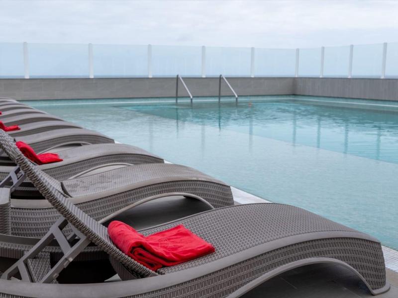 Zwembad met ligstoelen en rode handdoeken op een terras met uitzicht op zee.