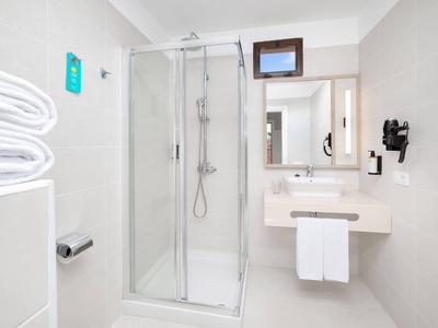 Helles Badezimmer mit Glasdusche, Waschtisch, Handtüchern und Haartrockner an der Wand.