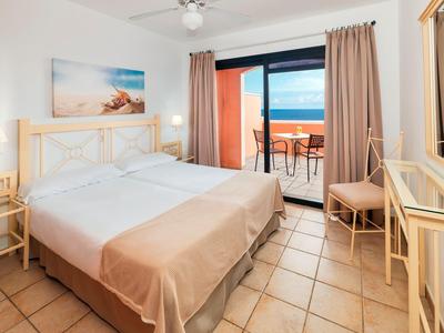 Helles Schlafzimmer mit Doppelbett, Fliesenboden, Balkon und Blick auf das blaue Meer.