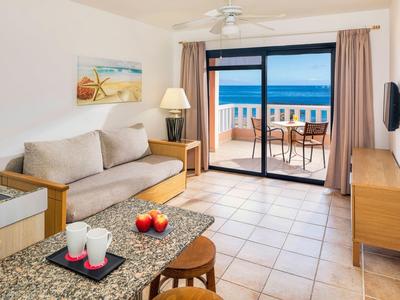 Helles Wohnzimmer mit beige Sofa, braunem Tisch, Terrasse und Meerblick durch große Glasfenster.