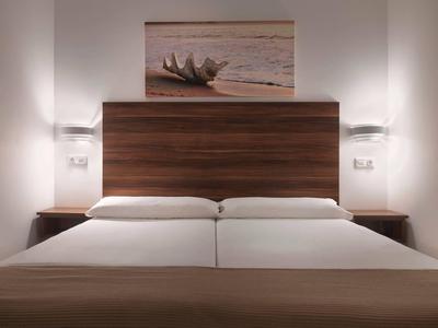Modernes Schlafzimmer mit zwei Betten, braunem Kopfteil und weicher Beleuchtung.