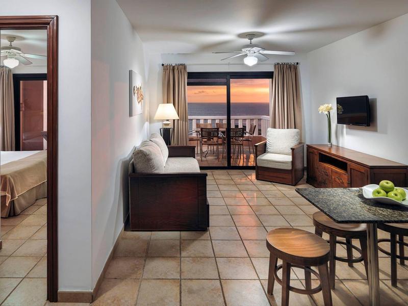 Moderní obývací pokoj s pohovkou, křeslem, jídelním stolem a terasou s výhledem na západ slunce.