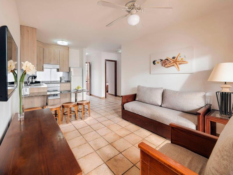 Světý obývací pokoj s pohovkou, konferenčním stolkem, otevřenou kuchyní a moderním designem.