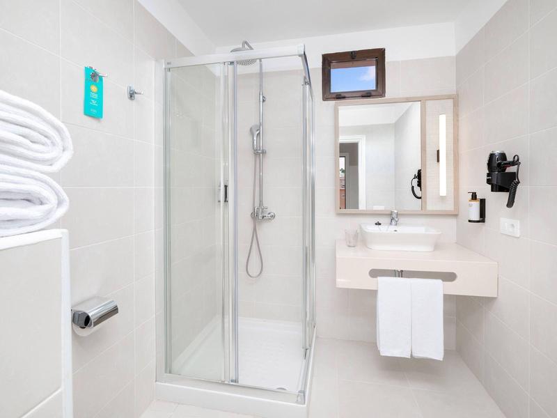 Moderní koupelna se skleněnou sprchou, bílými ručníky a umyvadlem se zrcadlem.