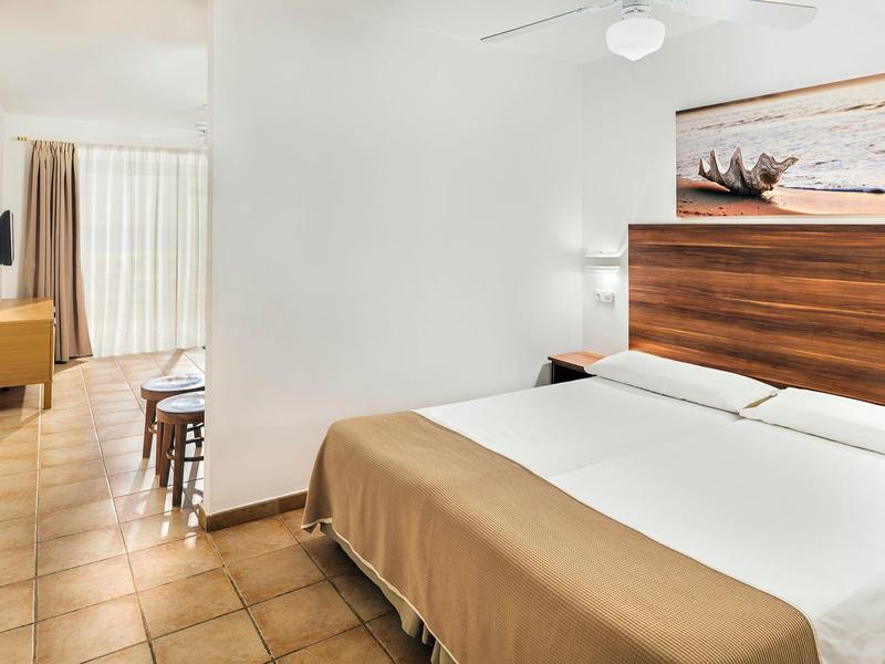 Moderní hotelový pokoj s velkou postelí, bílými stěnami a dlaždicovou podlahou.