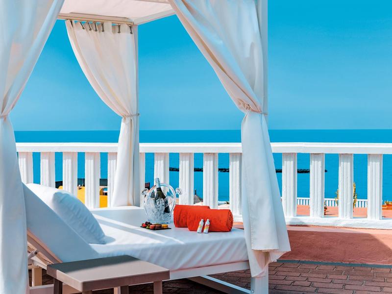 Luxusní terasa s bílým baliánským lůžkem s výhledem na moře pod modrou oblohou.