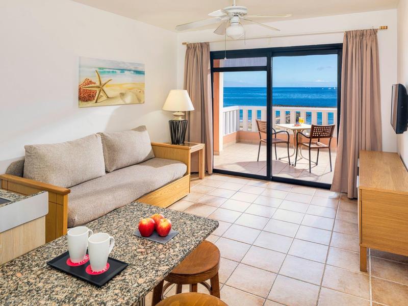 Světý obývací pokoj s pohovkou, stolkem, balkonem s výhledem na moře a moderním zařízením.