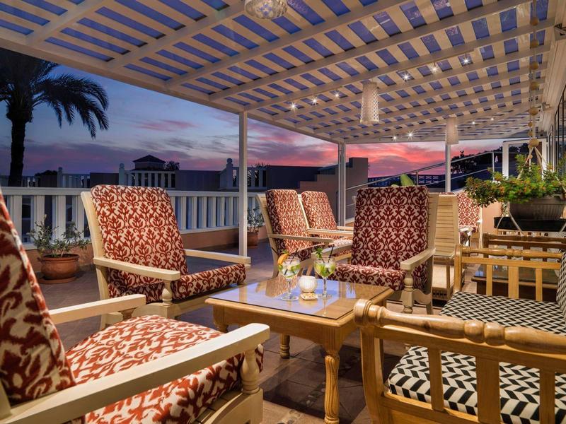 Noční terasa s pohodlnými židlemi a elegantním dekorem pod mřížkovou střechou.