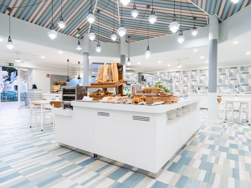 Panetteria moderna luminosa con scaffali bianchi e espositori di legno sotto soffitto a righe.