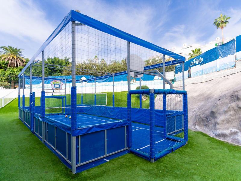 Recinto per trampolino blu su erba artificiale verde con palme sullo sfondo.