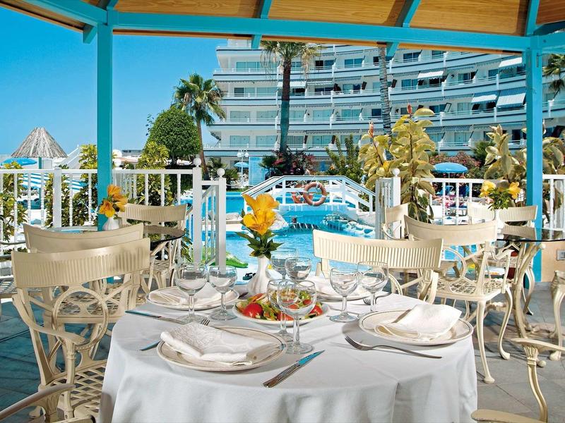 Restaurant terrace with set table overlooking hotel pool and palm trees.
