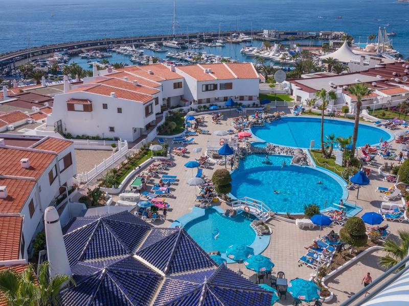 Coastal hotel with multiple pools, sun umbrellas, and a view of the marina.