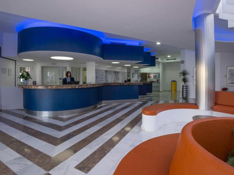 Modern hotel lobby with blue-lit reception desk and orange seating areas.