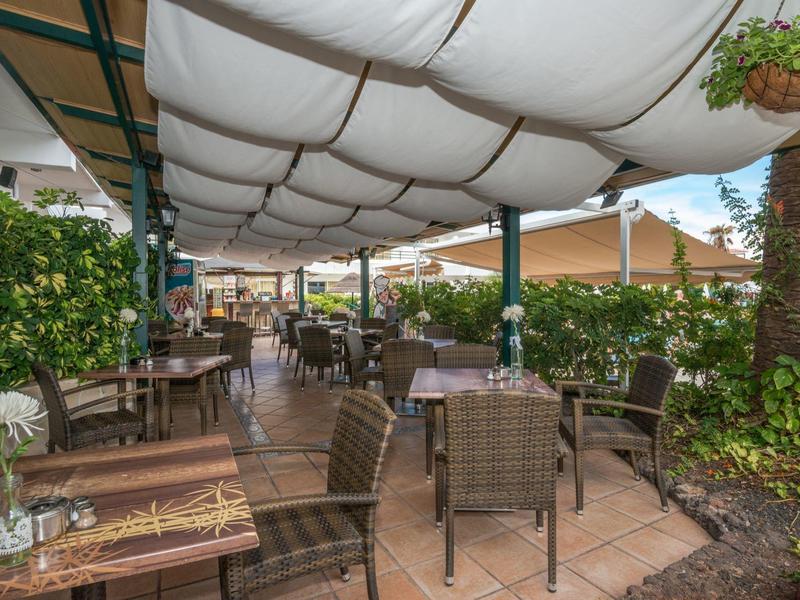 Widok na zadaszony taras z stolikami i krzesłami w hotelowym ogrodzie