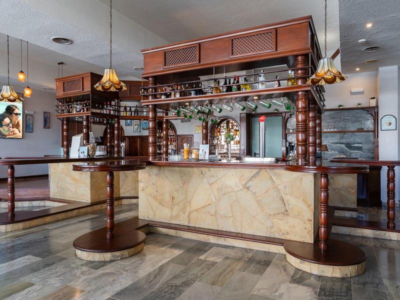 Hotelowy bar z marmurową ladą, wysokimi stołami i dekoracyjną drewnianą półką z butelkami