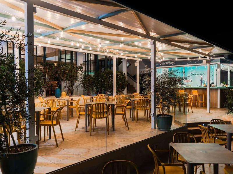 Oświetcony taras z drewnianymi stołami i krzesłami w hotelu nocą.