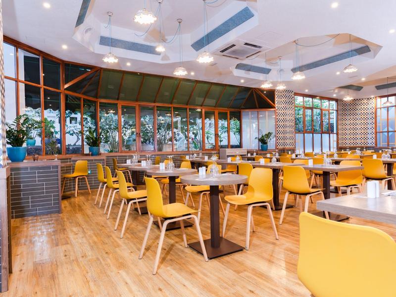 Jasna jadalnia z żółtymi krzesłami, drewnianą podłogą i dużymi oknami.