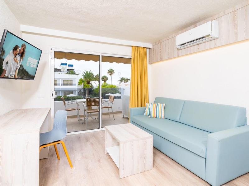 Jasny salon z niebieską sofą, telewizorem na ścianie i dostępem do tarasu z widokiem na zewnątrz.