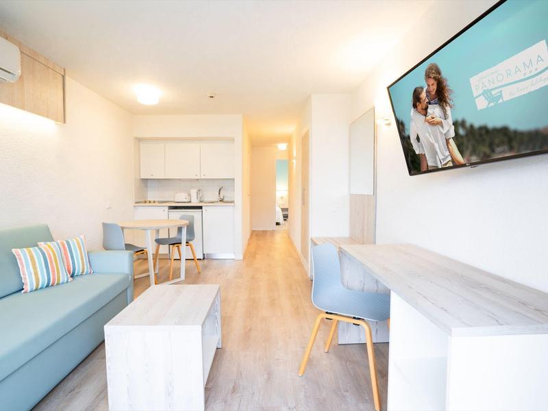 Jasny i nowoczesny pokój hotelowy z sofą, biurkiem i telewizorem na ścianie.