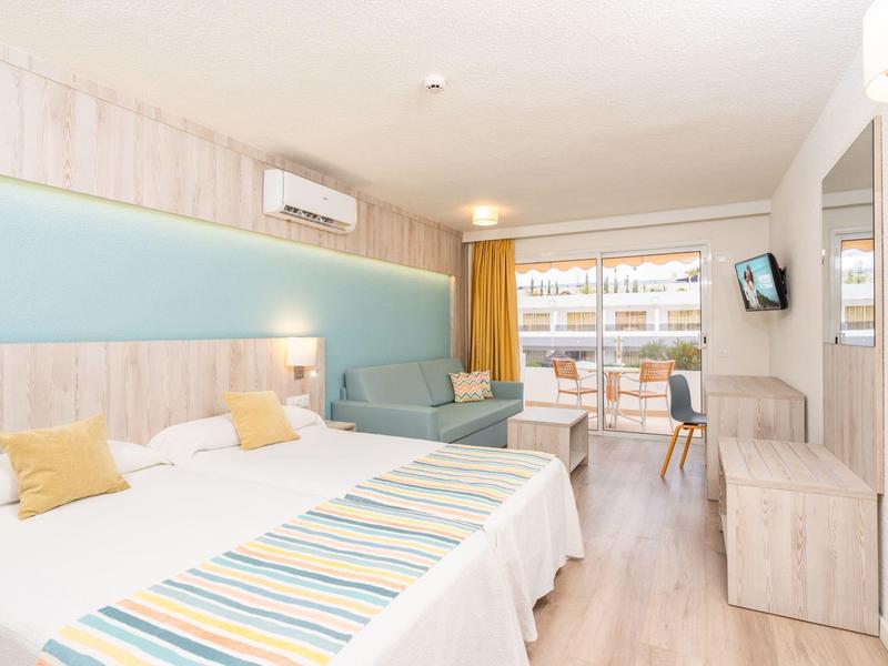 Nowoczesny pokój hotelowy z łóżkiem podwójnym, częścią wypoczynkową i balkonem z widokiem na morze.