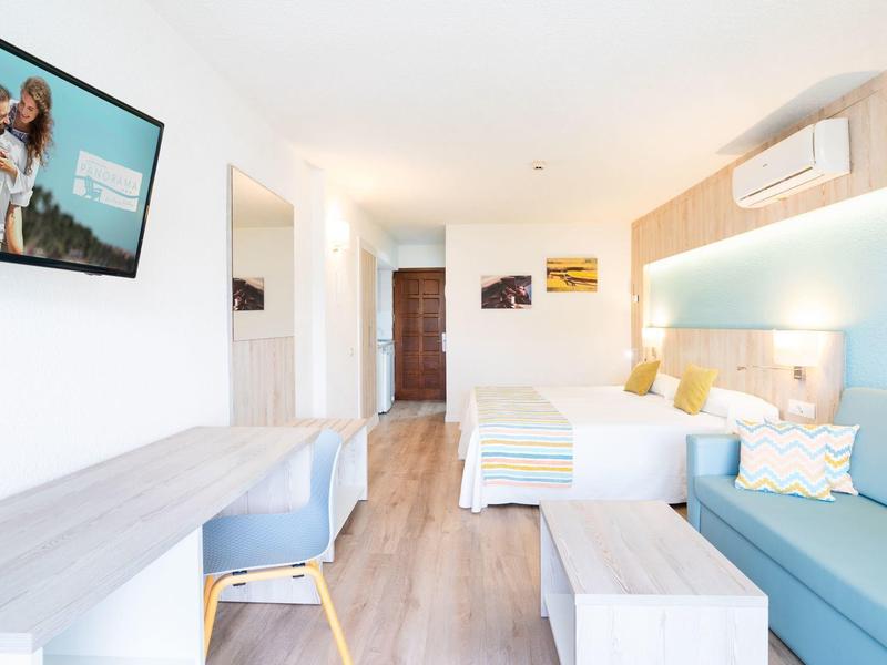 Jasny pokój hotelowy z łóżkiem podwójnym, sofą, biurkiem i nowoczesną dekoracją ścienną.