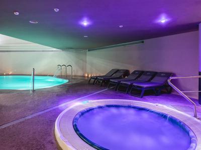 Moderner Wellnessbereich mit Whirlpool und Schwimmbecken, violettes Licht, Liegestühle an der Wand.