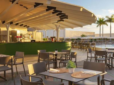 Moderner Außenbereich mit Tischen, Stühlen und Palmendekor neben einem Pool bei Sonnenuntergang.