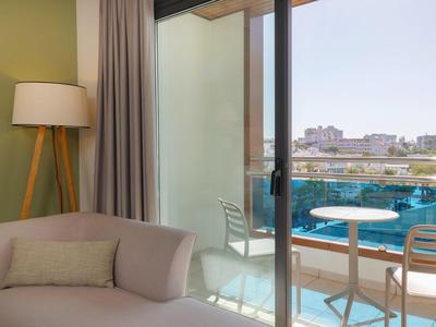 Modernes Hotelzimmer mit Sofa und Balkon mit Blick auf die Stadt und einen Pool.