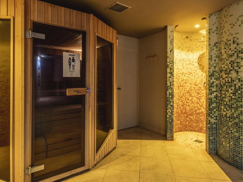 Moderner Wellnessbereich mit Holzsauna links und runder Duschkabine mit blauen Fliesen rechts.