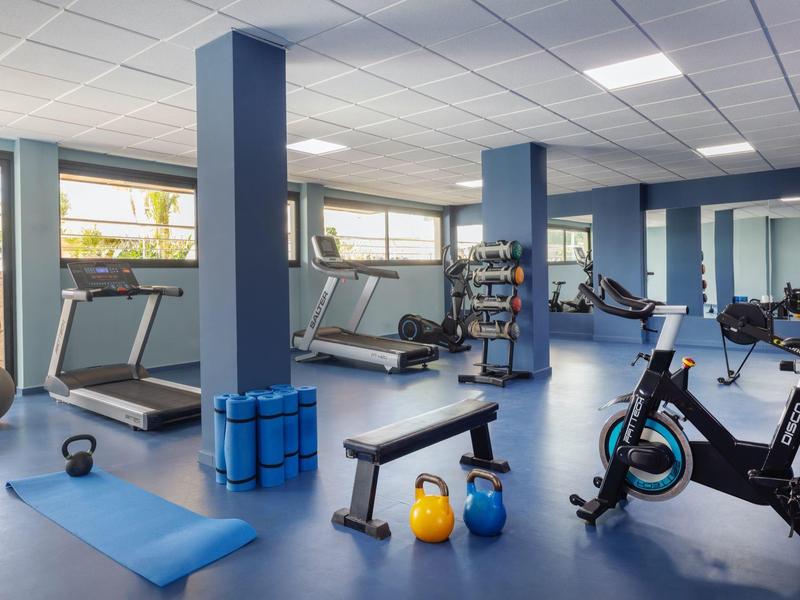 Moderne Fitnessraum mit Laufbändern, Fitnessgeräten, Hanteln und Yoga-Matte in hellem Raum.