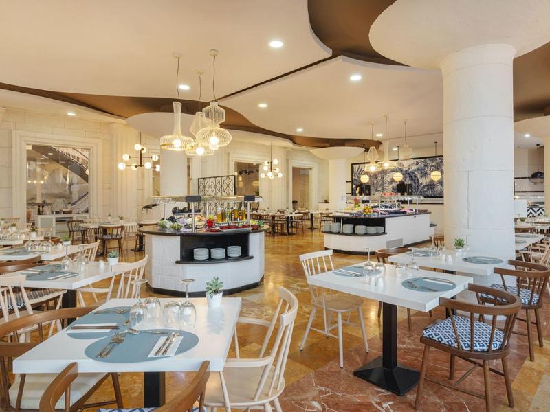 Helles Restaurant mit modernen Möbeln, weißen Stühlen, runden Lampen und organischem Deckendesign.