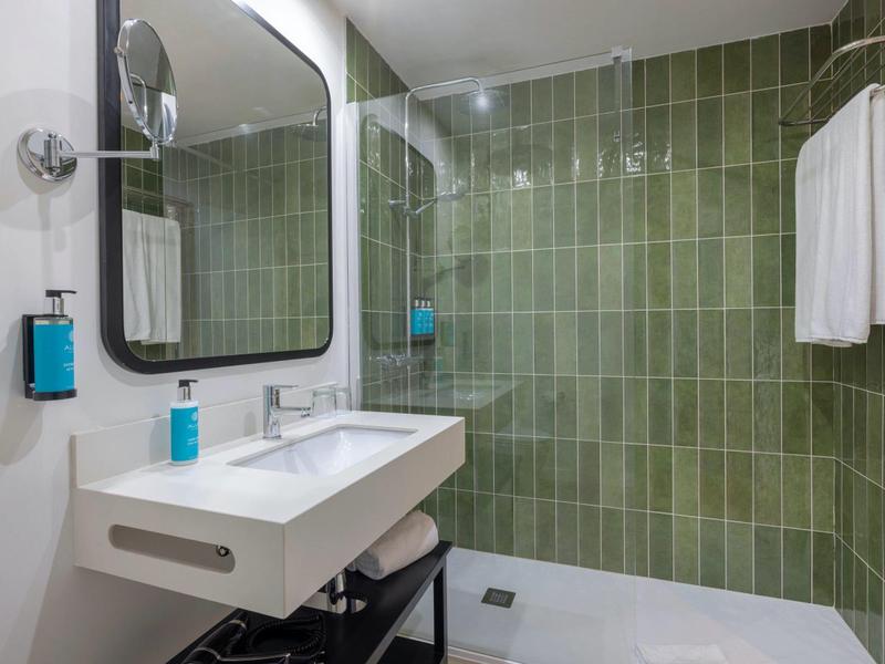 Modernes Bad mit grün gefliester Dusche, weißem Waschbecken und großem Spiegel.