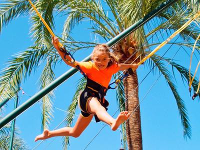 Dítě skáče na trampolíně pod palmami za jasné oblohy.