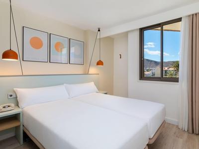 Helles Hotelzimmer mit großem Bett, modernen Lampen und Fenster mit Bergblick.