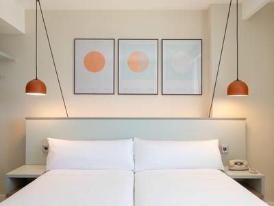 Modernes Schlafzimmer mit Doppelbett, weißen Kissen, Wandbildern und Hängelampen an beiden Seiten.