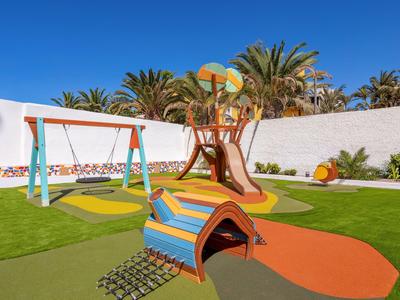 Colorful playground with slide and swing in a hotel area under a blue sky.