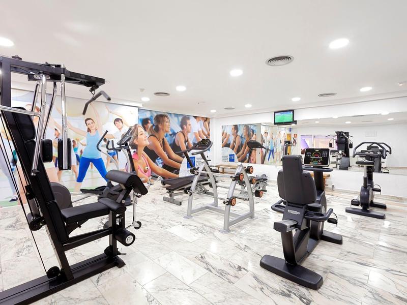 Moderner Fitnessraum mit verschiedenen Trainingsgeräten und farbenfrohen Wandbildern.