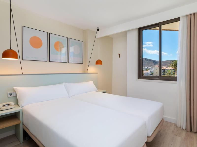 Helles Hotelzimmer mit großem Bett, modernen Lampen und Fenster mit Bergblick.