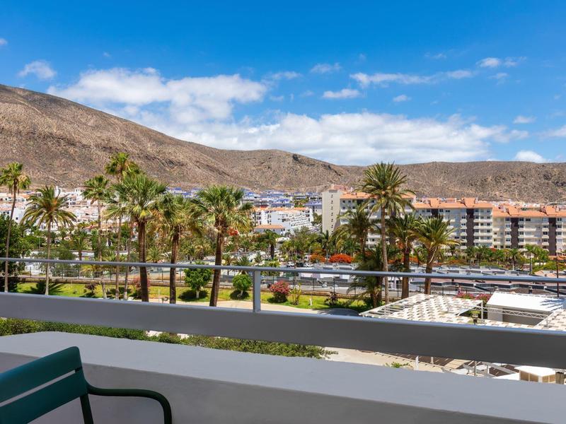 Blick auf Palmen und Gebäude vor einem gebirgigen Hintergrund bei blauem Himmel.