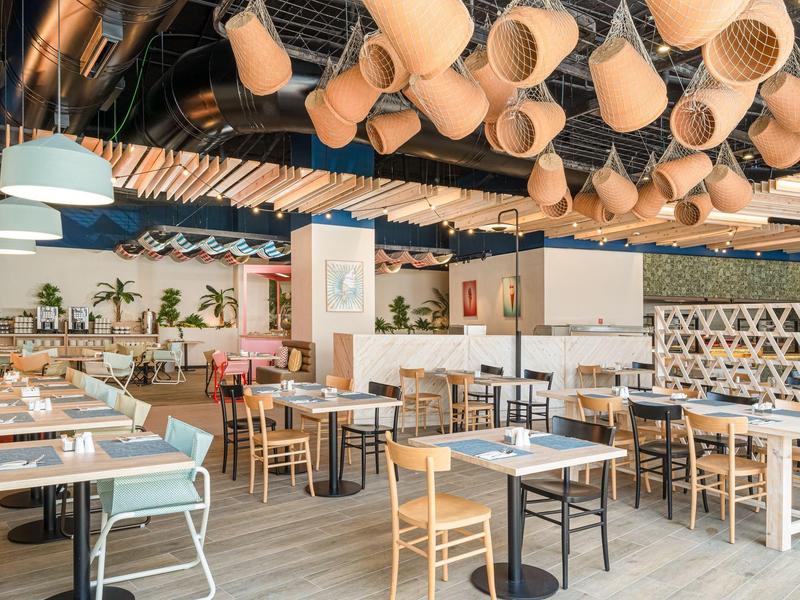 Restaurant moderne avec chaises en bois, tables et éléments décoratifs suspendus au plafond.
