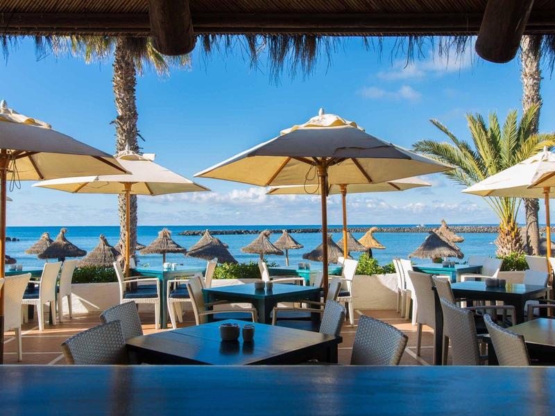 Restaurant en plein air avec parasols blancs et vue sur la mer par temps clair.