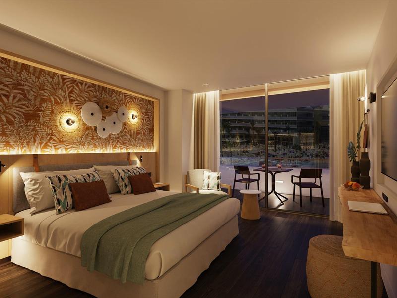 Chambre d'hôtel élégante avec grand lit, éclairage chaleureux et balcon avec sièges.