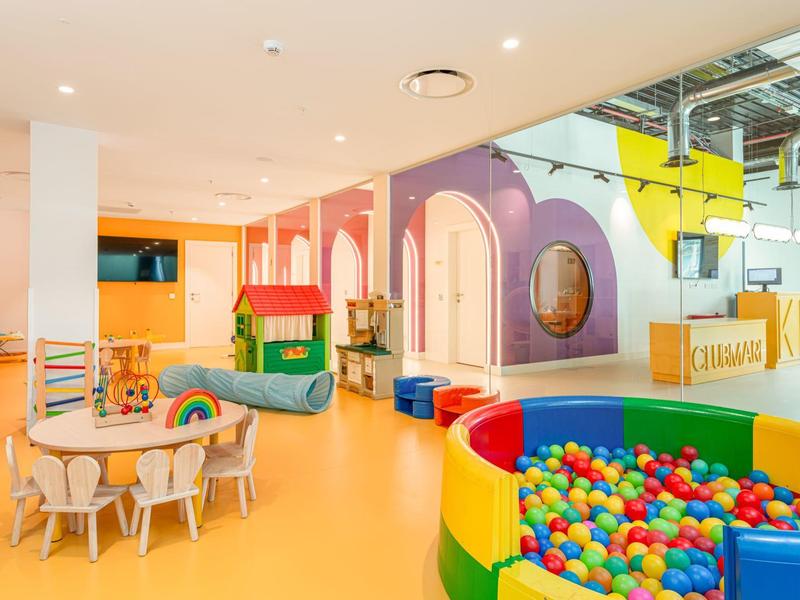 Espace de jeux intérieur coloré avec piscine à balles, petites tables, chaises et structures de jeu vibrantes.