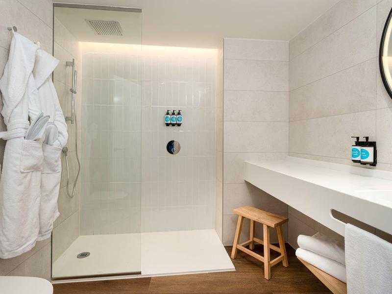 Salle de bain moderne avec grande douche, tabouret en bois et miroir éclairé