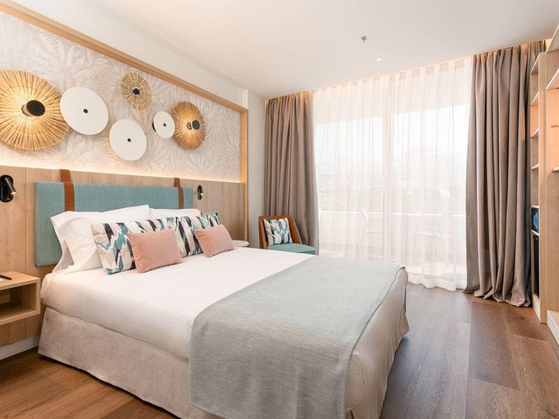 Chambre d'hôtel moderne avec lit double, éléments décoratifs muraux et fenêtres du sol au plafond.