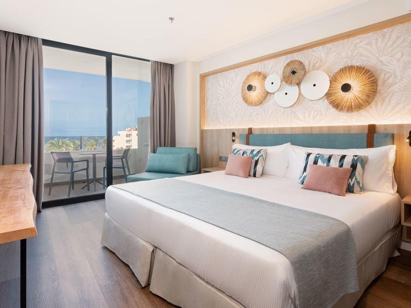 Chambre d'hôtel moderne avec lit double, coin salon et balcon surplombant la mer.